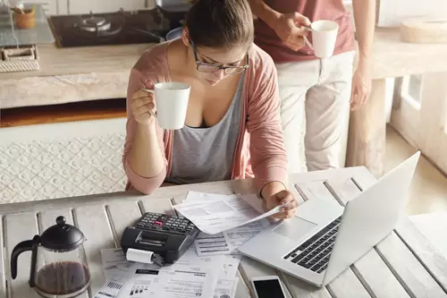 Empreendedora organizando contas e documentos ao lado de um notebook e uma calculadora