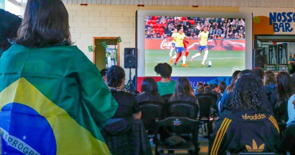 Clientes reunidos em um bar assistindo a um jogo de futebol em um telão